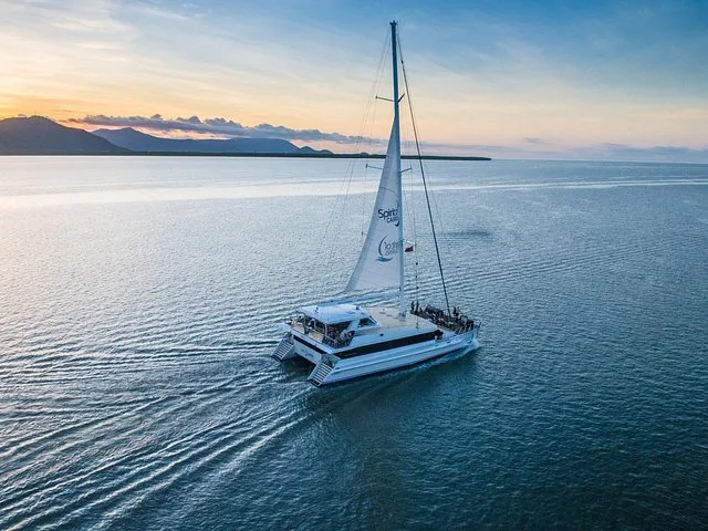 Catamaran sailing on Trinity Inlet at sunset with mountains in the background