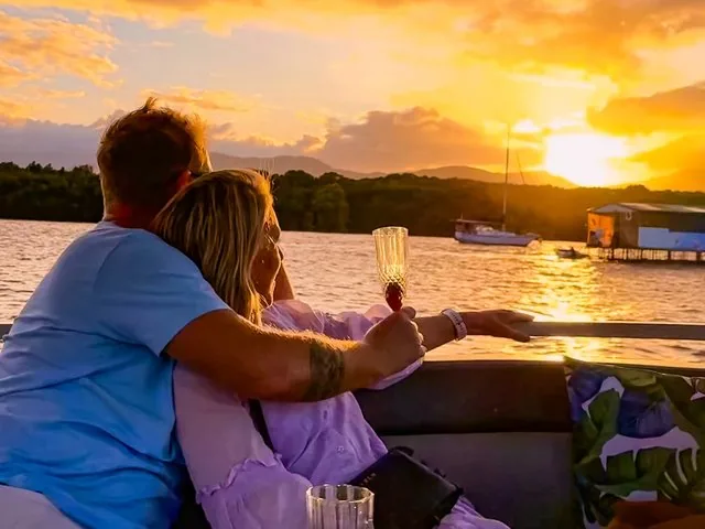 Ein Paar, das sich auf einem Boot umarmt und bei Sonnenuntergang ein Getränk genießt.