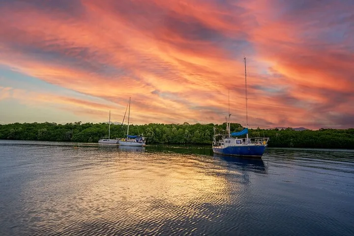 Several sailboats anchored in calm water under a vibrant sunset sky.