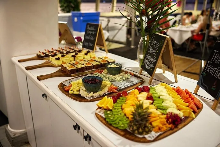 Buffet table with fruit platters, cheese boards, and small cakes on wooden boards