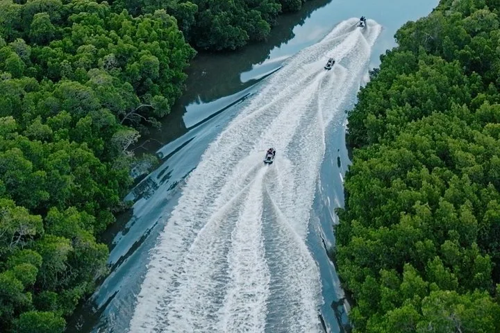 Aerial view of three personal watercraft speeding along a river between mangroves.